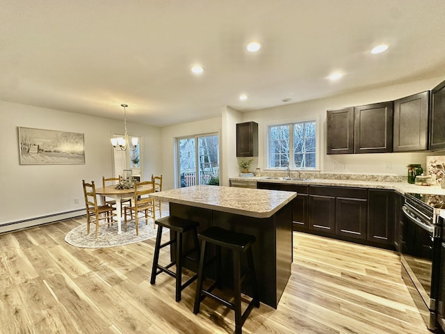 kitchen featuring hanging light fixtures, light wood-type flooring, stainless steel electric range oven, a kitchen island, and sink