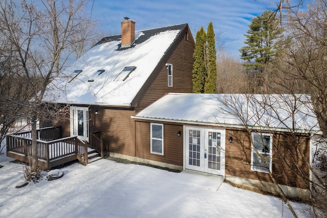 snow covered house with a deck and french doors