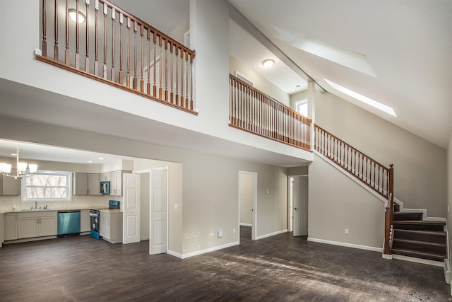 unfurnished living room featuring a skylight, dark wood-type flooring, sink, high vaulted ceiling, and a chandelier