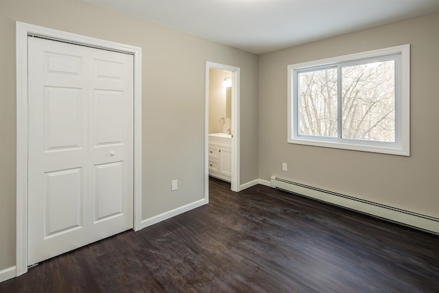 unfurnished bedroom featuring baseboard heating, ensuite bathroom, a closet, and dark hardwood / wood-style floors