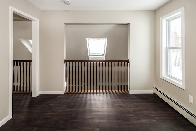 unfurnished room featuring a skylight, dark wood-type flooring, and a baseboard heating unit