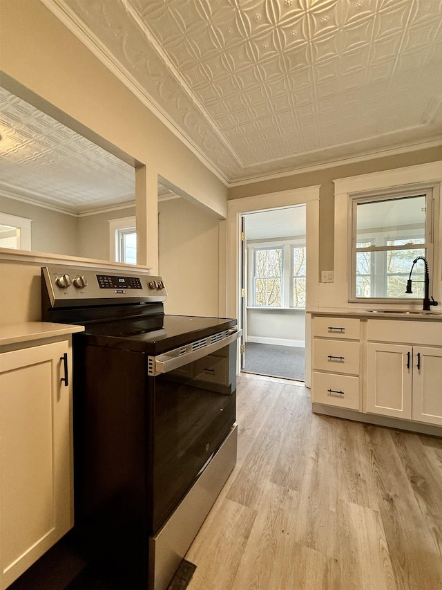 kitchen featuring sink, light hardwood / wood-style flooring, ornamental molding, stainless steel electric range oven, and white cabinetry