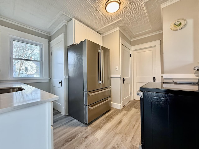 kitchen with white cabinets, ornamental molding, high quality fridge, light hardwood / wood-style floors, and range