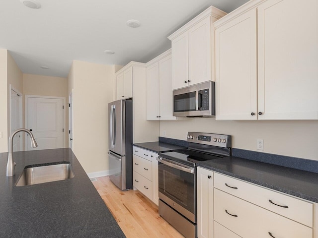 kitchen with light hardwood / wood-style floors, white cabinetry, sink, and appliances with stainless steel finishes