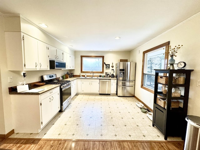 kitchen with white cabinets, appliances with stainless steel finishes, ornamental molding, and sink