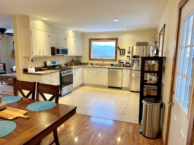 kitchen featuring appliances with stainless steel finishes, light wood-type flooring, ornamental molding, sink, and white cabinetry