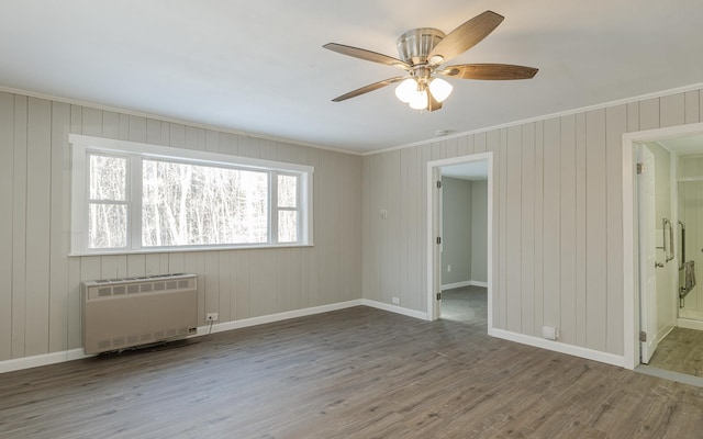 empty room featuring hardwood / wood-style flooring, ceiling fan, wood walls, and radiator