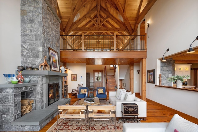 living room featuring hardwood / wood-style floors, high vaulted ceiling, wooden ceiling, and a stone fireplace