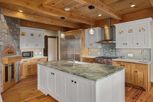 kitchen with white cabinets, premium appliances, a kitchen island with sink, and wall chimney range hood