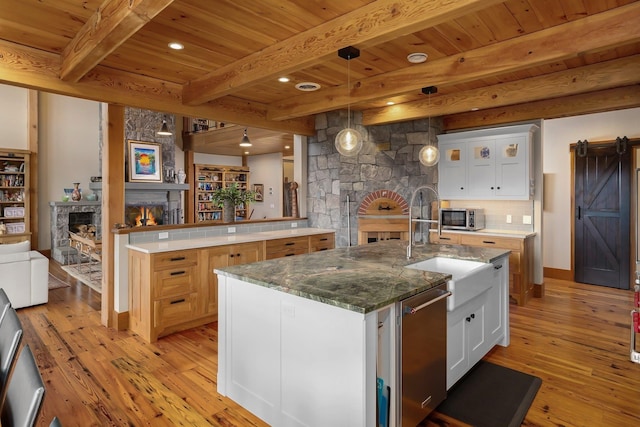 kitchen with beamed ceiling, white cabinetry, a fireplace, and an island with sink