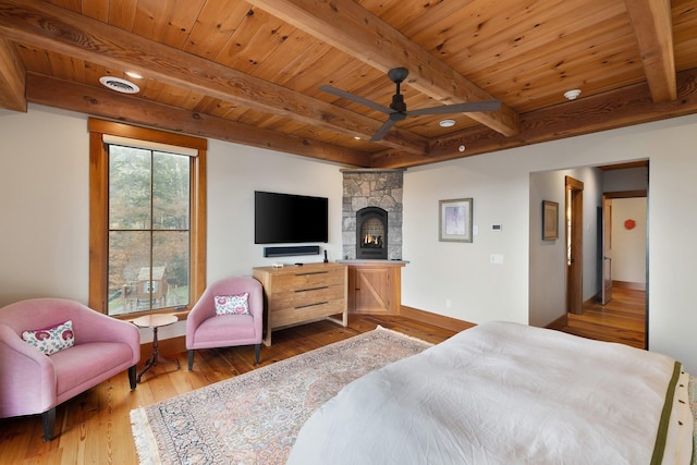 bedroom featuring hardwood / wood-style floors, a stone fireplace, beam ceiling, and wood ceiling