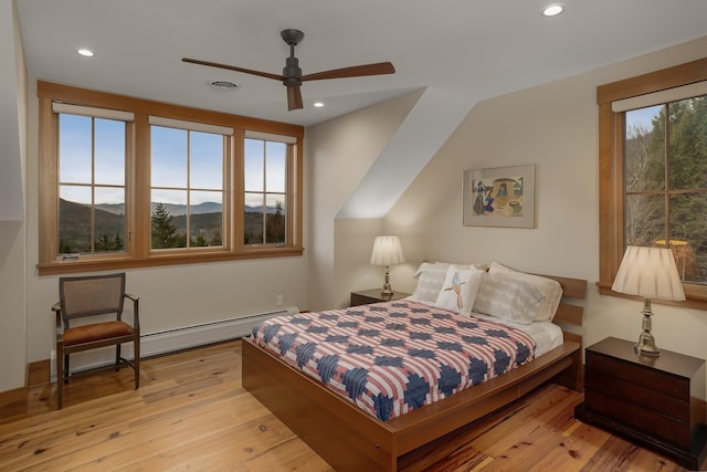 bedroom featuring a mountain view, ceiling fan, a baseboard radiator, and light wood-type flooring