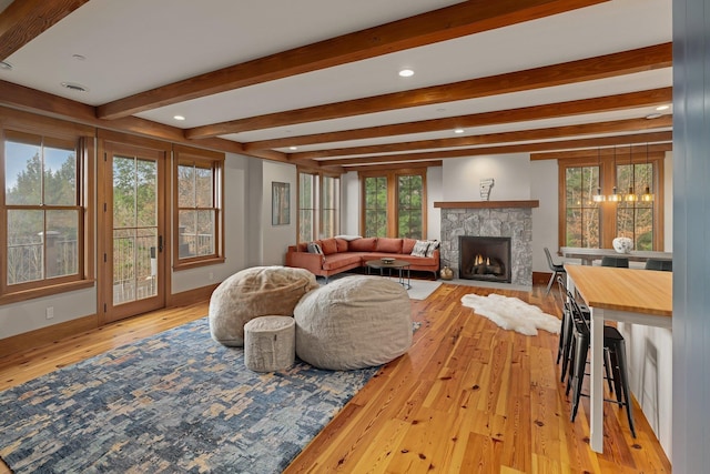 living room with beam ceiling, a stone fireplace, a wealth of natural light, and light hardwood / wood-style flooring