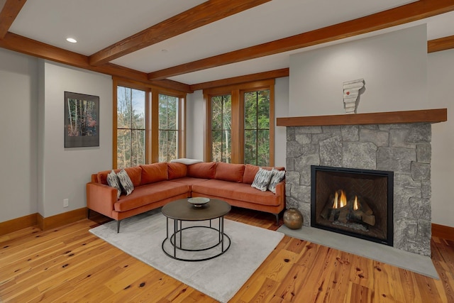 living room with beam ceiling, a stone fireplace, and light wood-type flooring