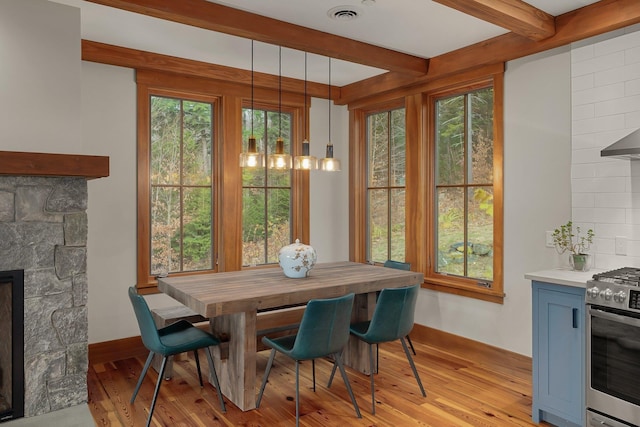 dining space with a wealth of natural light, a fireplace, beamed ceiling, and light wood-type flooring