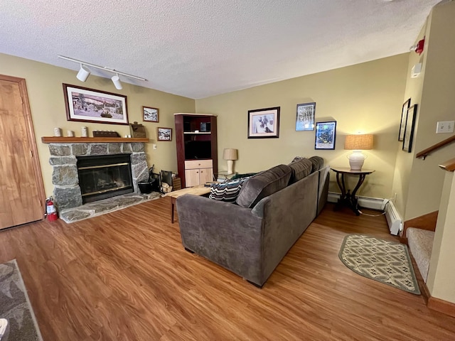 living area featuring a stone fireplace, stairway, a textured ceiling, and wood finished floors