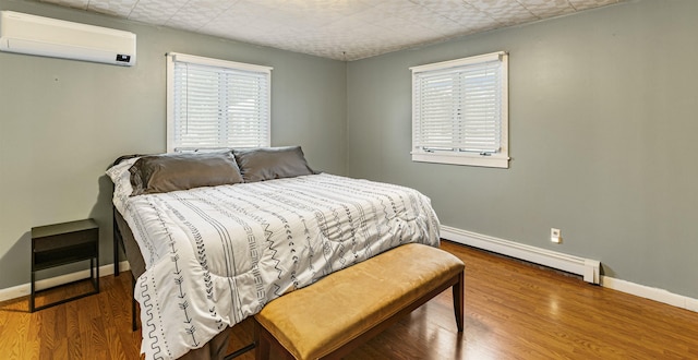 bedroom with a wall mounted AC, hardwood / wood-style flooring, and baseboard heating