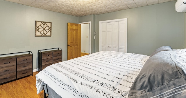 bedroom with a wall mounted air conditioner, light wood-type flooring, and a closet