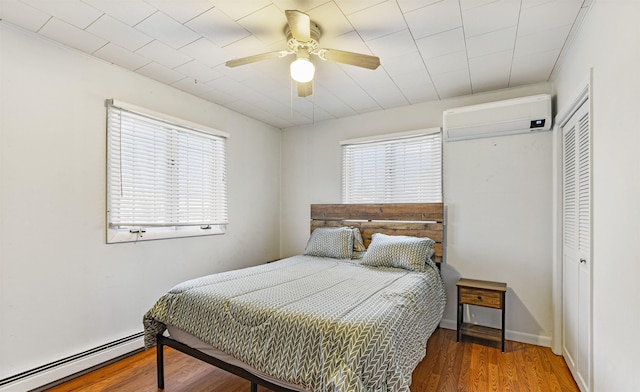 bedroom with ceiling fan, baseboard heating, dark hardwood / wood-style flooring, a wall mounted AC, and a closet