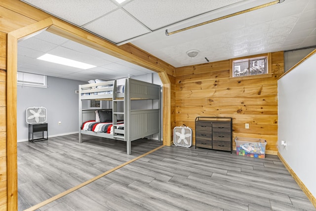 unfurnished bedroom with wood walls, a drop ceiling, and light hardwood / wood-style floors