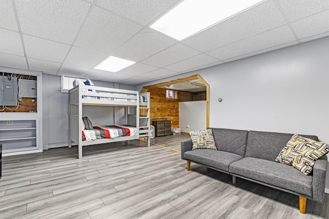 living room with a paneled ceiling, hardwood / wood-style flooring, wooden walls, and electric panel