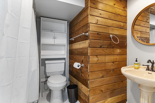 bathroom featuring curtained shower, wooden walls, sink, and toilet