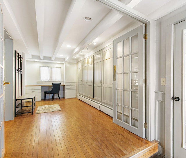 interior space with baseboard heating, beamed ceiling, built in desk, and light wood-type flooring