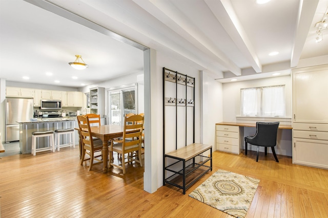 dining space with beam ceiling, built in desk, and light hardwood / wood-style flooring