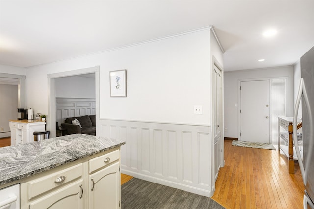 kitchen with light stone counters, a baseboard heating unit, stainless steel fridge, cream cabinets, and wood-type flooring