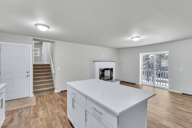 kitchen with baseboard heating, light stone counters, light hardwood / wood-style flooring, and white cabinets