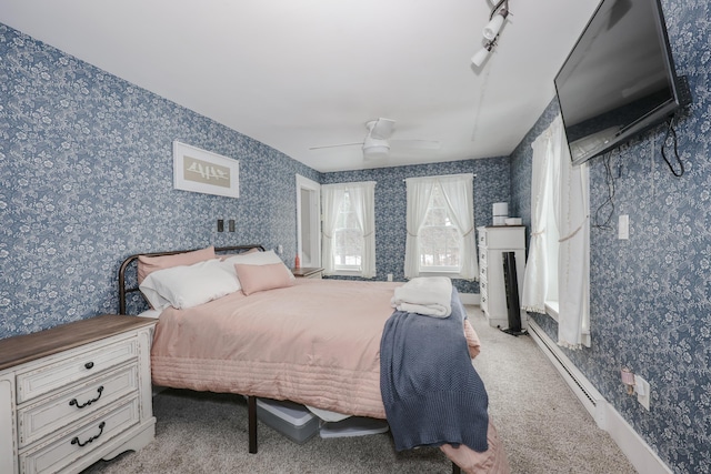 carpeted bedroom with rail lighting, ceiling fan, and a baseboard heating unit