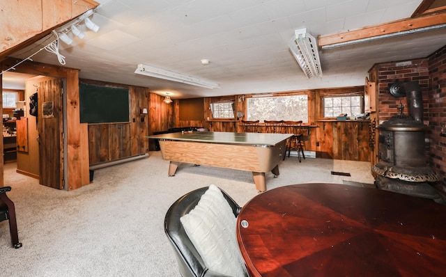 game room with a wood stove, light carpet, a baseboard radiator, and wood walls