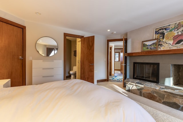 carpeted bedroom featuring connected bathroom, a closet, and a stone fireplace