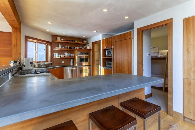 kitchen featuring appliances with stainless steel finishes, stainless steel counters, light hardwood / wood-style floors, kitchen peninsula, and a breakfast bar area