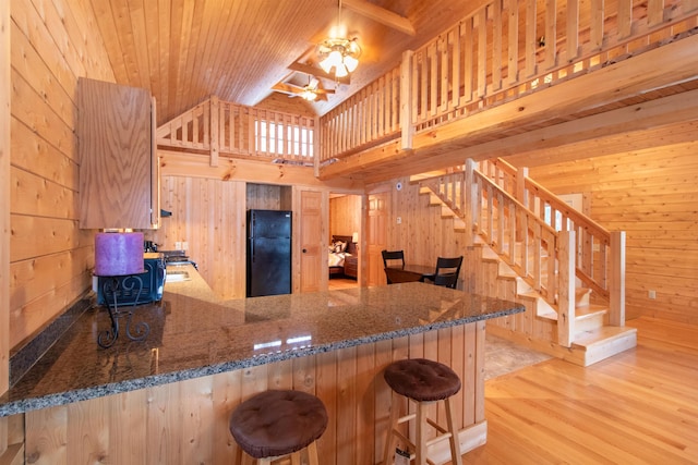 kitchen featuring wooden walls, dark stone counters, wooden ceiling, freestanding refrigerator, and a peninsula