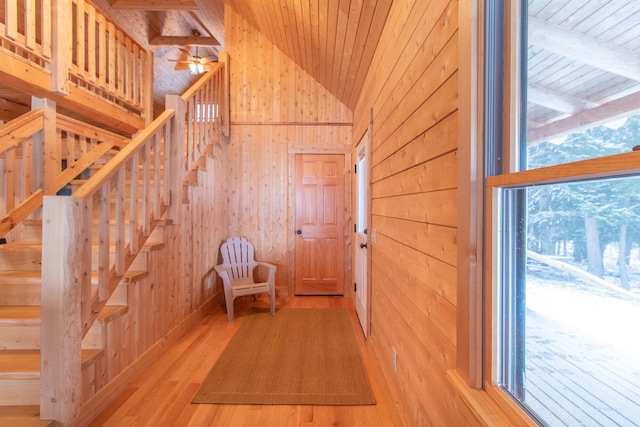 hallway with lofted ceiling, light wood-style flooring, wood ceiling, wood walls, and stairs