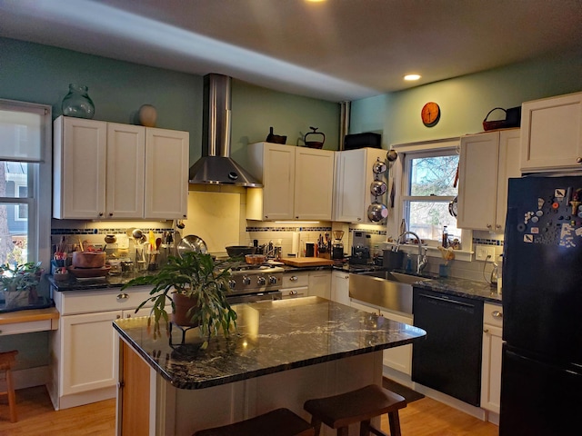 kitchen featuring wall chimney exhaust hood, sink, black appliances, white cabinets, and a kitchen island