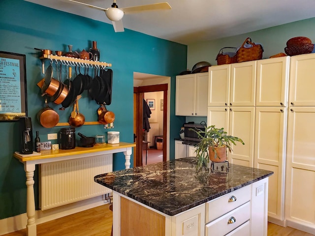 kitchen featuring light wood-type flooring, dark stone counters, ceiling fan, radiator heating unit, and a center island