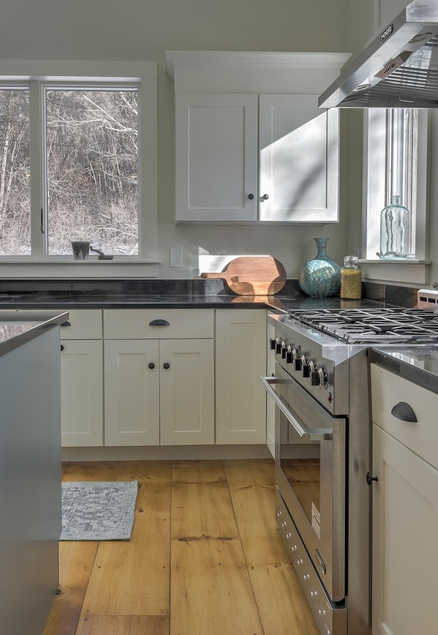 kitchen with white cabinetry, extractor fan, stainless steel range, and light hardwood / wood-style floors