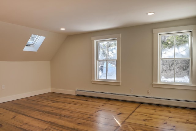 additional living space with a baseboard radiator, vaulted ceiling with skylight, and light hardwood / wood-style floors