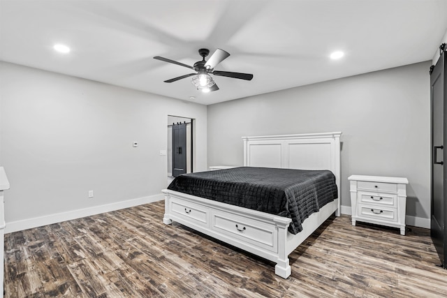 bedroom featuring ceiling fan, a barn door, and dark wood-type flooring