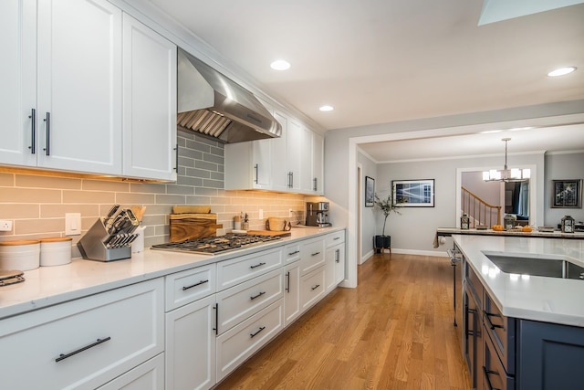 kitchen with wall chimney exhaust hood, stainless steel gas cooktop, light wood-type flooring, pendant lighting, and white cabinets