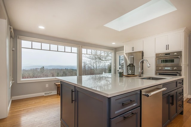 kitchen featuring light hardwood / wood-style flooring, white cabinetry, a kitchen island with sink, a skylight, and a mountain view