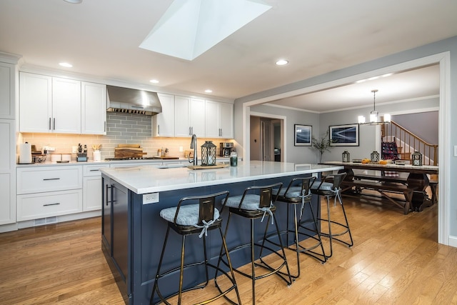 kitchen featuring a spacious island, wall chimney exhaust hood, a kitchen bar, decorative light fixtures, and white cabinets