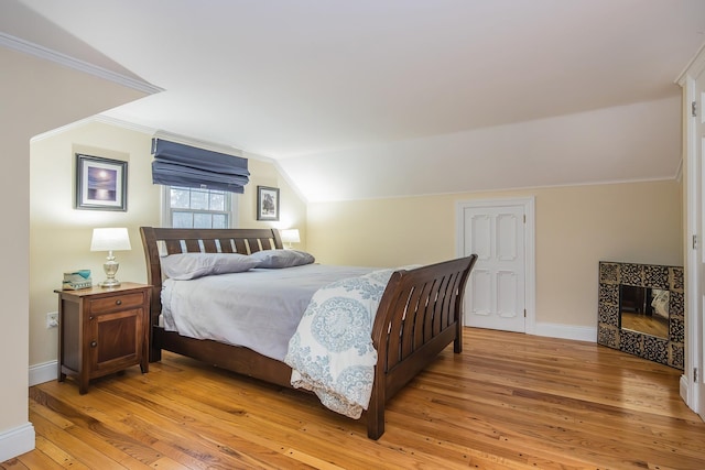 bedroom featuring a tile fireplace, ornamental molding, lofted ceiling, and light wood-type flooring