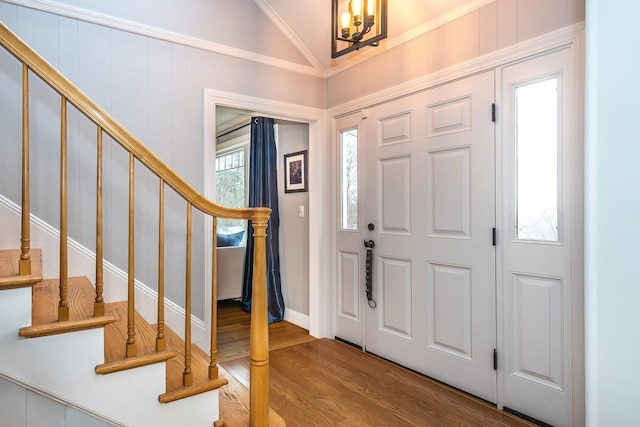 foyer entrance featuring lofted ceiling, a notable chandelier, wood-type flooring, and ornamental molding