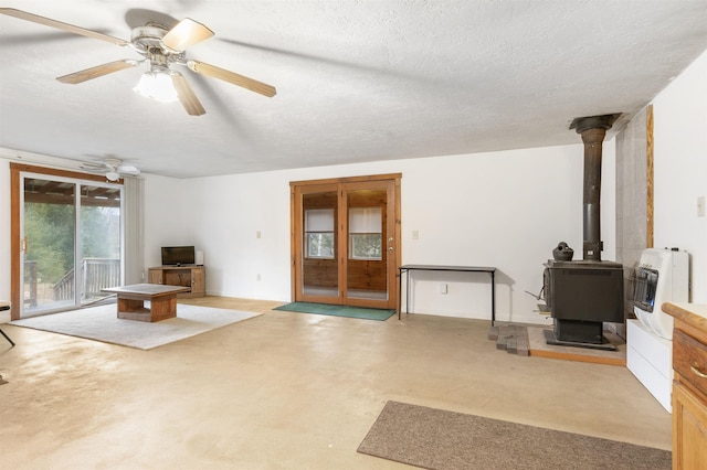 living room with ceiling fan, a wood stove, a textured ceiling, and heating unit