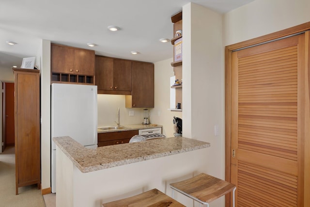 kitchen with sink, light stone countertops, white fridge, a kitchen bar, and kitchen peninsula