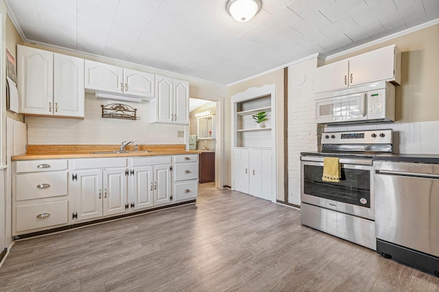 kitchen with appliances with stainless steel finishes, sink, built in features, light hardwood / wood-style flooring, and white cabinetry