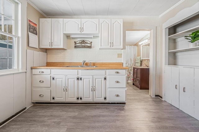 kitchen featuring wood counters, light wood-type flooring, ornamental molding, sink, and white cabinetry